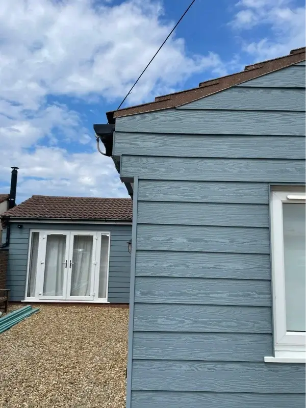 Blue-grey horizontal cladding fitted to a bungalow with white-framed windows and French doors. By Norfolk Exterior Solutions.
